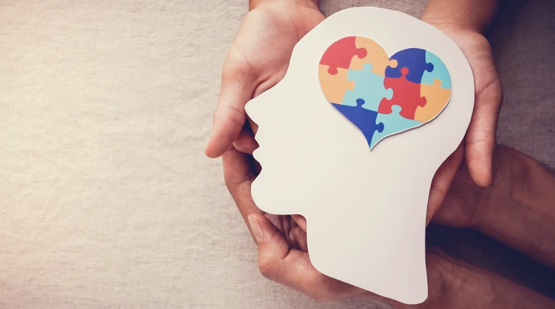 Dłonie trzymające papierowy kształt głowy z sercem ułożonym z kolorowych puzzli