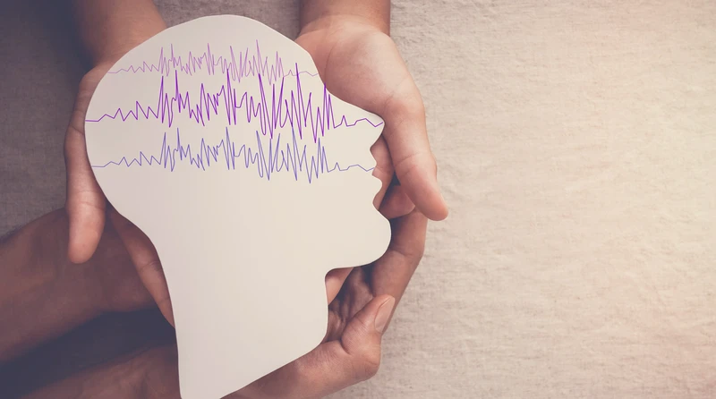 Dłonie trzymające papierowy kształt głowy z liniami przypominającymi fale mózgowe